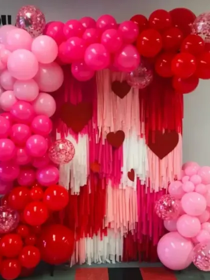 Get ready for love! This Valentine's Day backdrop features a red and pink streamer wall framed by a lush balloon arch with heart accents, perfect for a romantic celebration.