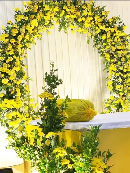 A simple and bright Haldi backdrop, featuring a floral arch made entirely of yellow flowers, perfect for intimate home ceremonies.