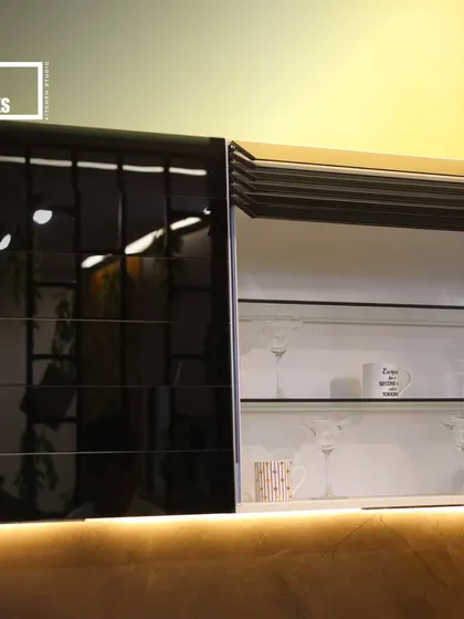This cabinet features a combination of a glossy black lift-up door and a roller shutter, revealing glass shelves for storing glassware. The under-cabinet light illuminates the counter and adds to the modern feel.