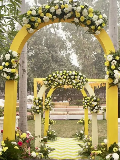A classic yellow floral archway welcomes guests to a traditional Haldi ceremony, set in a beautiful garden. The bright yellow is cheerful and perfectly suited for the occasion.