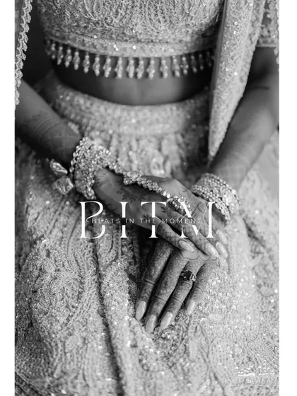 A detailed black and white shot of the bride's hands, adorned with henna and bangles, resting on her intricately embroidered lehenga. It's a portrait of tradition and elegance.
