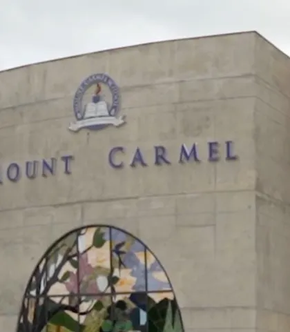 A close-up of the Mount Carmel school logo and name on the exposed concrete facade, just above the large stained glass window.