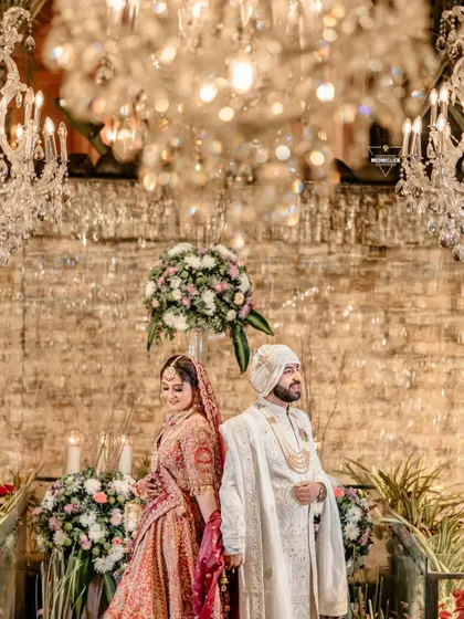 A regal portrait of the couple standing back-to-back under stunning crystal chandeliers, creating a look of timeless elegance.