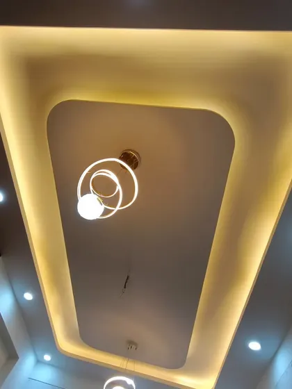 A finished false ceiling with a simple rectangular design and cove lighting. The hanging decorative light adds a final touch of elegance.