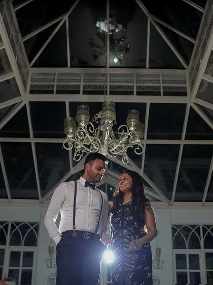 A wide-angle shot of a couple during their pre-wedding shoot inside a beautiful glasshouse. The architectural details and dramatic lighting create a sophisticated and elegant atmosphere.