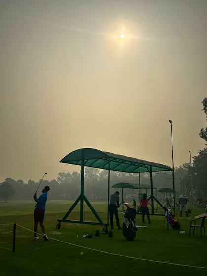 A golfer takes a powerful swing as the sun burns through the morning haze.