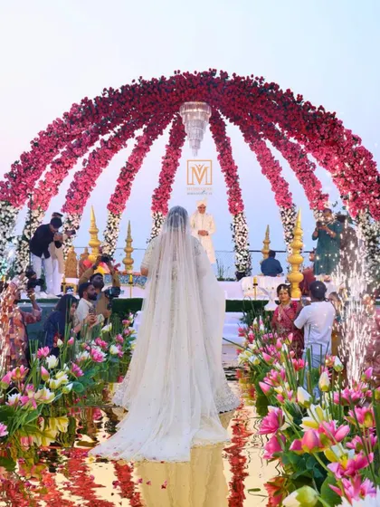 A bride's grand entrance to a stunning sea-facing mandap. The aisle is designed with a mirrored surface and floating lotuses, creating the illusion of walking on water towards a floral dome.