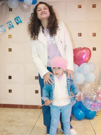 A mother and child pose for a full-length shot at a birthday party, showing off their coordinated casual outfits.