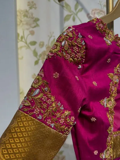 A close-up of the sleeve of the magenta and gold blouse, showcasing the detailed floral embroidery with silver and pink threads.