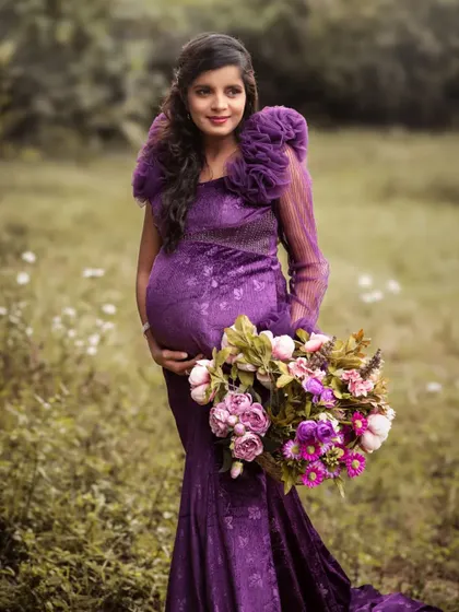 A stunning solo portrait in a field of wildflowers. The mother-to-be, in a dramatic purple gown, holds a large bouquet, looking like a queen of the meadow.
