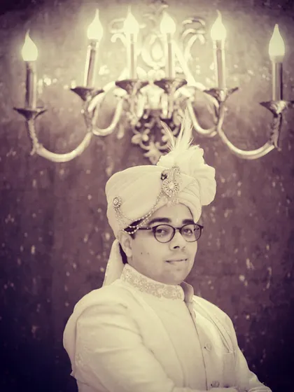 A classic groom portrait with a vintage, royal feel. The warm, focused lighting on the groom's sherwani and sehra, set against the ornate candelabra, creates a timeless and regal image that honors tradition.