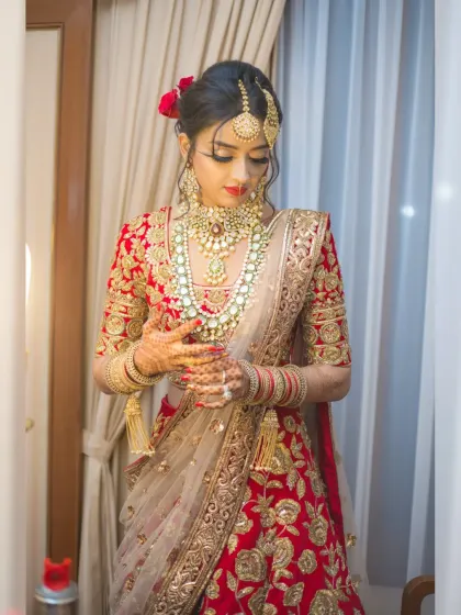 A bride adjusts her jewelry in a moment of quiet preparation. This full-length shot captures the elegance of her red lehenga and the final touches before the ceremony.