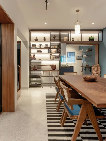 The dining room is the heart of the Keepsake home, featuring a large 8-seater table that encourages gathering. It is surrounded by open shelves displaying the client's artifacts, blending life, travel, and design into a single, cohesive narrative.
