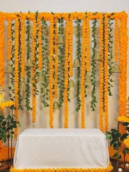 A simple yet beautiful marigold wall decoration for a puja or Haldi ceremony at home. The hanging temple bells and lanterns add a divine and traditional touch to the setup.
