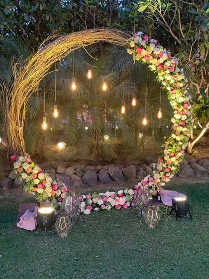 This rustic twig arch, decorated with fresh flowers and hanging Edison bulbs, creates a magical photo point for an evening Mehndi or Haldi function. It's a beautiful blend of natural and modern elements.