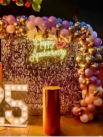 An outdoor rooftop setup for a 25th anniversary. The decor features a silver shimmer wall, a balloon arch, and large marquee numbers.