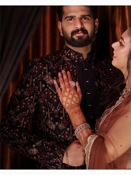 A close-up on the bride's hand on the groom's chest, showcasing her ring and the intricate detail of his sherwani.