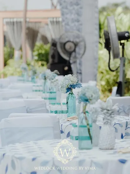 The details of our tropical pool party decor. The tables featured custom blue and white linens, with centerpieces of white-painted pineapples and blue-tinted water bottles holding fresh flowers.