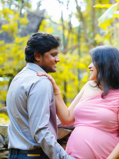 A candid moment between a couple during their outdoor maternity shoot. The natural light and green surroundings create a warm and peaceful atmosphere.