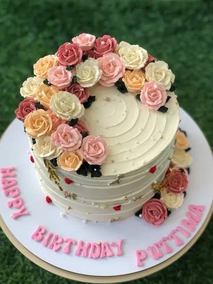 A beautiful birthday cake with a cascade of hand-piped buttercream roses in a warm, sunset-inspired color palette.