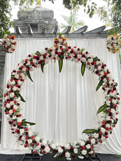 This circular floral arch is one of our most popular designs for receptions and engagements. It creates a stunning photo backdrop using a mix of red, white, and orange flowers, blending modern style with traditional elements.