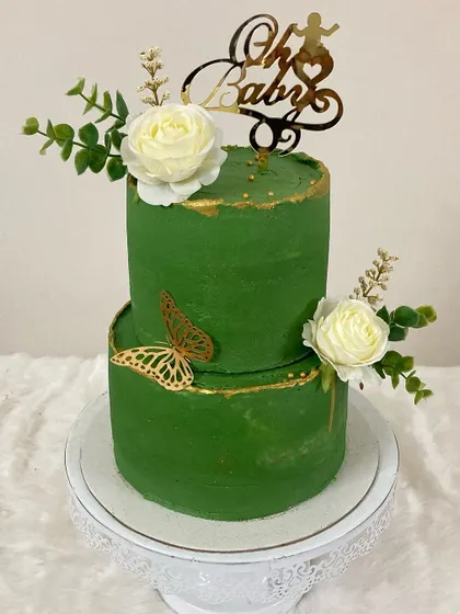 An elegant two-tier baby shower cake in a rich emerald green. The design is accented with golden butterflies and delicate white sugar roses for a sophisticated look.