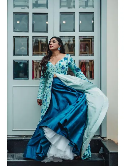 A contemporary fusion wear portrait. This image showcases a stylish lehenga with a long floral jacket, capturing the flow and structure of the outfit against a modern architectural backdrop.