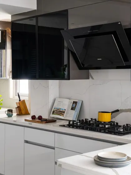 A close-up of the cooking area, featuring a black angled chimney and hob set against a white quartz backsplash. The design is clean and uncluttered, with every inch crafted for clarity and ease of use.