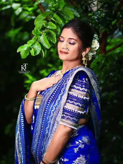 A serene outdoor shot of a bride in a royal blue Paithani saree. The natural light highlights the flawless makeup and the intricate details of her attire.