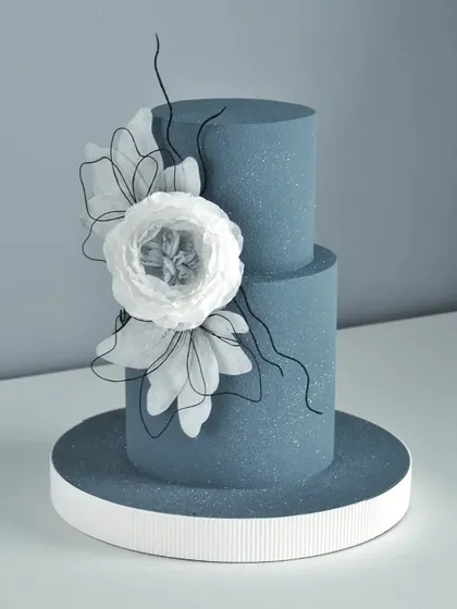 A pretty two-tiered blue cake with a glitter finish and a large, handcrafted white wafer paper flower.