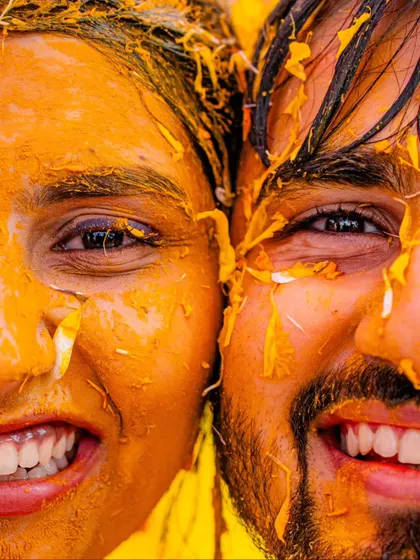 A super close-up shot capturing the happy, turmeric-covered faces of the bride and groom. This image is all about the texture, the vibrant color, and the infectious smiles.