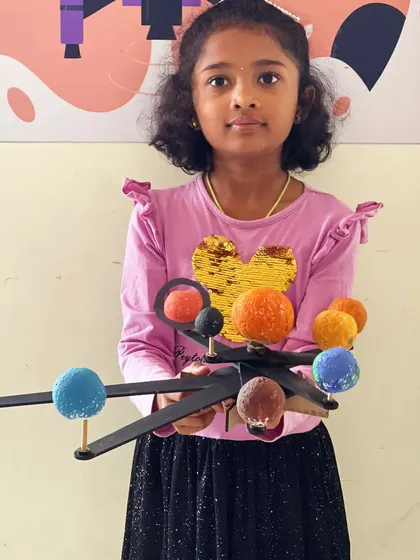 A young astronomer holds up the solar system model she carefully assembled and painted.