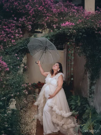 A joyful moment captured in a light shower. The transparent umbrella adds a playful element while the mother-to-be looks up, embracing the moment.
