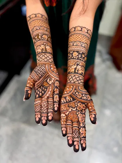 A traditional bridal mehendi featuring a procession of elephants on the forearms. The palms have a mix of floral and geometric patterns.