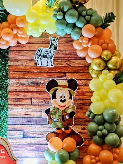 A Mickey Mouse safari theme detail, showing Mickey in his explorer outfit as part of a balloon arrangement against a wood and hedge backdrop.