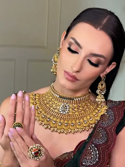 The final touches make all the difference. Here, the model admires the complete look, with perfectly blended eyeshadow, radiant skin, and glossy lips that tie together the entire traditional ensemble.