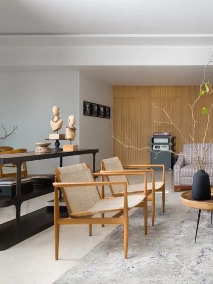 This angle showcases the mix of seating, including light wood and rattan armchairs that add a layer of natural texture against the distressed area rug and the sleek, dark console table.