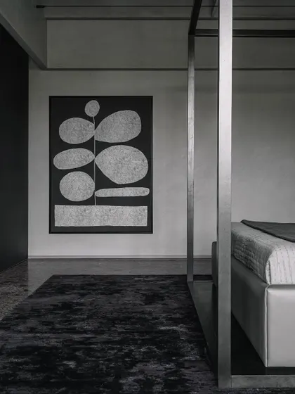 A detail of the art and material textures in the Vaulted Haus master bedroom. The monochrome artwork complements the dark rug and the metal frame of the four-poster bed, creating a sophisticated, layered composition.