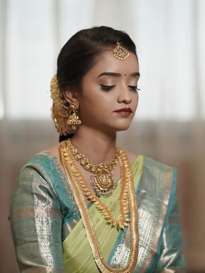 A serene moment from a daylight Muhurtham. The makeup is minimal and elegant, with a focus on a flawless base and soft eye makeup to complement her beautiful silk saree.