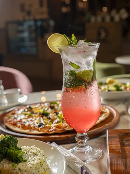 A complete meal setting with a refreshing pink mocktail, pizza, and pasta. This type of shot is perfect for restaurants wanting to showcase the variety and ambiance of their dining experience.