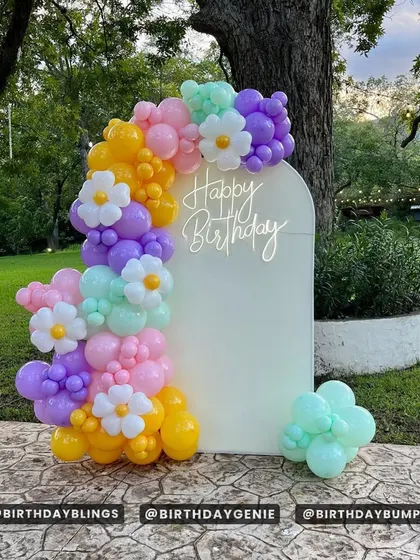 A cheerful and colorful balloon garland on a white arched backdrop. The mix of pastel purple, pink, yellow, and mint, along with daisy-shaped balloons, is perfect for a spring or summer party.