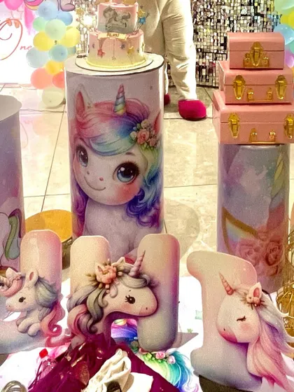 A detailed shot of the unicorn-themed decor, showing custom-printed plinths, a unicorn-themed cake, and large, sculpted letters spelling 'RUHI'.