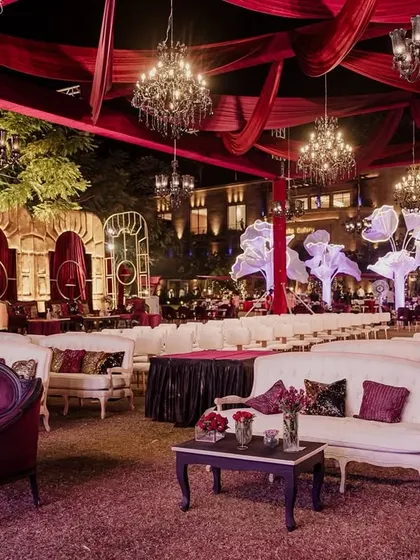 A sweeping view of 'The Scarlet Soirée' for Aashvi and Akash. The venue is bathed in rich red tones, with elegant lounge seating, dramatic draping, and large, illuminated floral trees creating a romantic and opulent atmosphere.