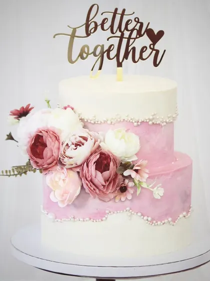 An elegant two-tiered cake designed for a beautiful beginning. The combination of pink watercolor buttercream and clean white tiers is accented with pearl details and a cascade of fresh, beautiful peonies.