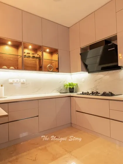 An L-shaped modular kitchen that perfectly blends function and style. The space features handle-less glossy cabinets, a marble-effect backsplash, and a compact, foldable breakfast table for quick meals.