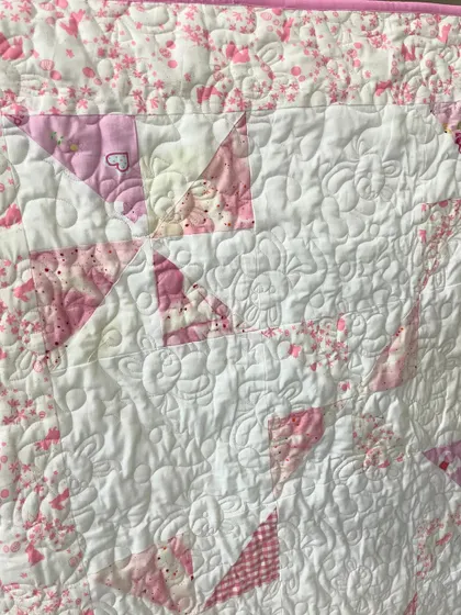 A close-up of the pink pinwheel baby quilt, highlighting the dense, floral longarm quilting.