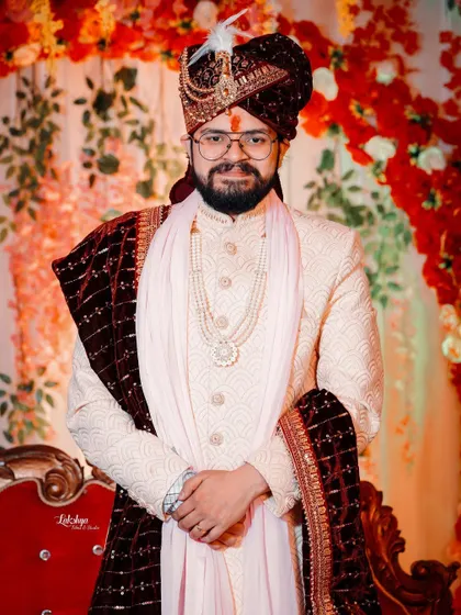A full-length portrait of the groom looking regal in his wedding attire. The floral background adds a touch of color and celebration to his elegant look.