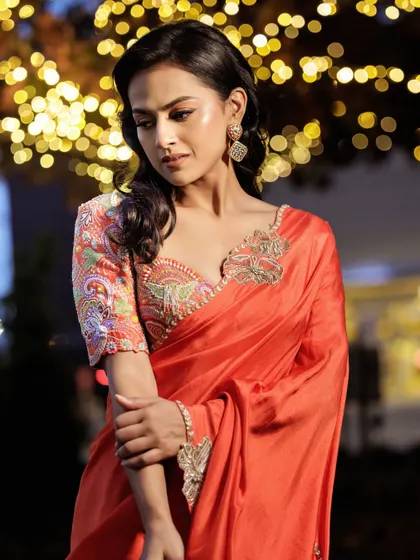 The beautiful details of the multi-colored threadwork on the blouse of this orange saree. It’s a great way to add a pop of color to a classic drape.