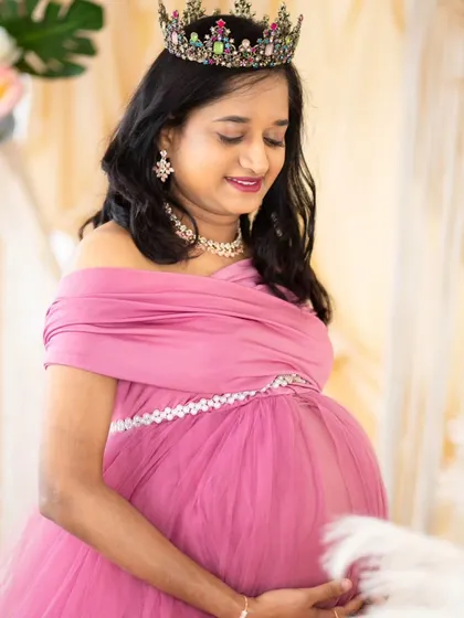 A soft and delicate portrait. The mom-to-be, wearing a pink gown and crown, looks down at her bump with a gentle smile, capturing the tender emotions of pregnancy.