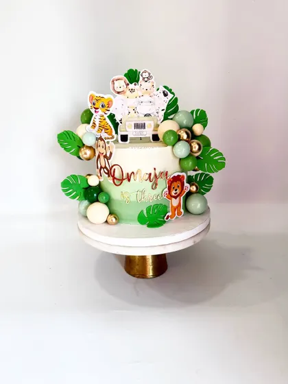 This view shows the balance of the printed animal toppers, chocolate spheres, and fondant leaves, creating a vibrant and festive look for a third birthday.